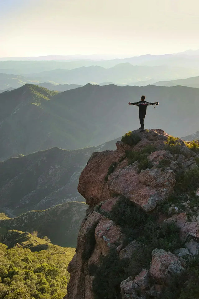 Silhouetted figure embracing resilience on rocky cliff edge