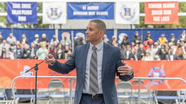 School leader in grey suit gestures at podium, driving community engagement via Avodah Dynamics