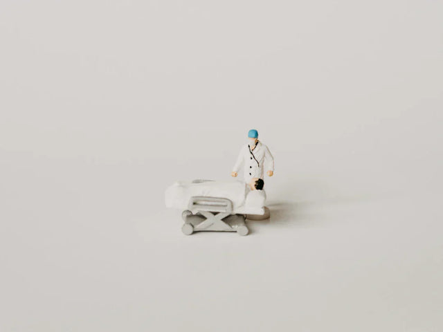 Miniature doctor figurine beside hospital gurney illustrating celebrating small wins and success