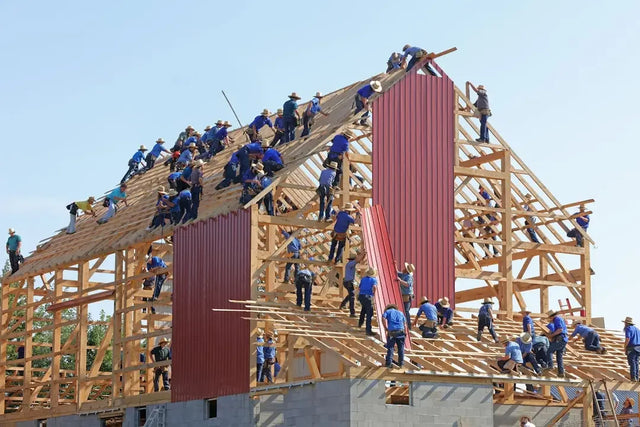 Construction workers in blue shirts enhancing company culture through teamwork on barn roof.