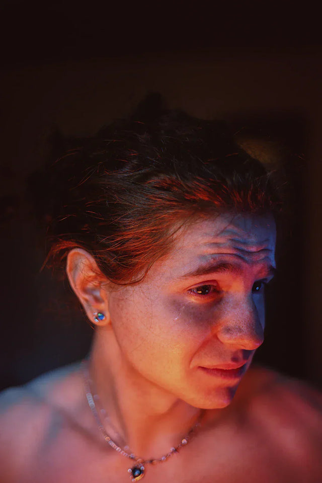 Person with reddish-brown hair and distressed expression wearing silver necklace with blue charm, embodying embracing vulnerability for authentic connections