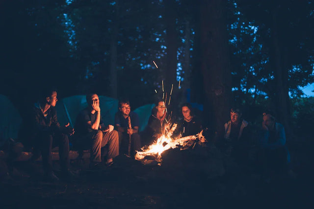Group of people around a campfire at night demonstrating storytelling techniques with foam trucker hats