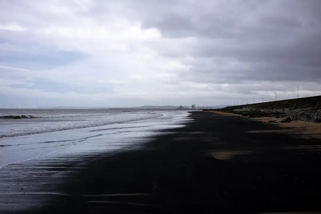 Dark volcanic beach along a moody coastline symbolizes change management for team members.