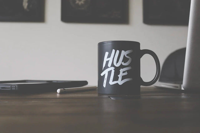 Black ceramic coffee mug with HUSTLE in white script symbolizing hustle culture and focus