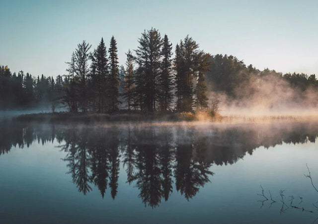 Misty lake with tree-covered island at sunrise representing active lifestyle and lifestyle apparel