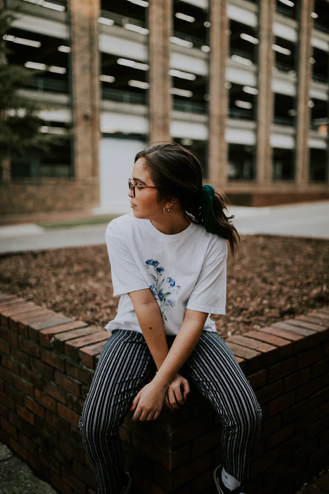 Young woman with glasses and green hair tie wearing a white t-shirt with blue floral design, illustrating setting personal goals for clarity and motivation