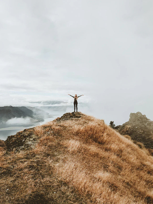 Person standing triumphantly on grassy mountain peak symbolizing positive mindset and achievable goals