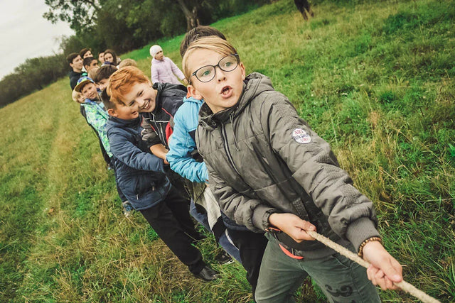 Group of people playing tug-of-war on a grassy slope illustrating strong school leadership