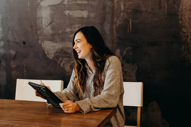 Woman in grey shirt laughing while using tablet, exemplifying taking risks for leadership growth