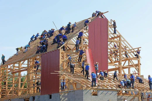 Construction workers in blue shirts installing roof trusses and siding, exemplifying effective team collaboration
