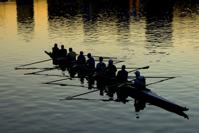 Crew team rowing an eight-person shell on calm water at sunset for effective collaborative campaigns