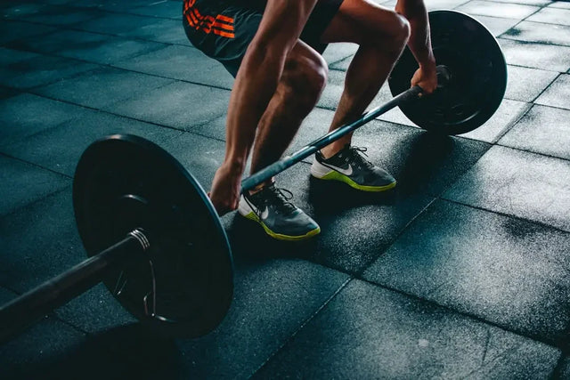Athlete gripping loaded barbell at floor level for balanced health amid hustle culture