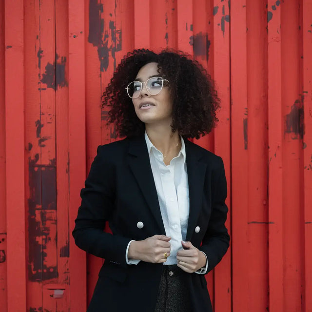 Woman in black suit against red wall representing hustle culture and healthy work-life balance.