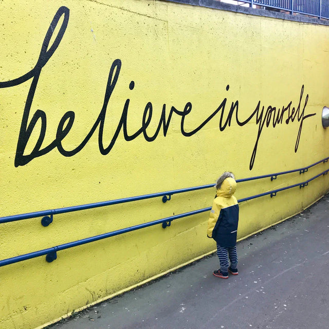 Child standing in front of a yellow wall symbolizing breaking limiting beliefs and growth mindset