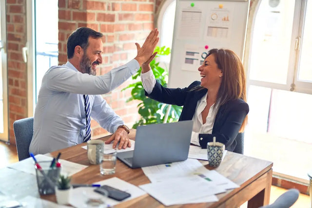 Coworkers celebrating a positive work culture with a high-five at their desks.