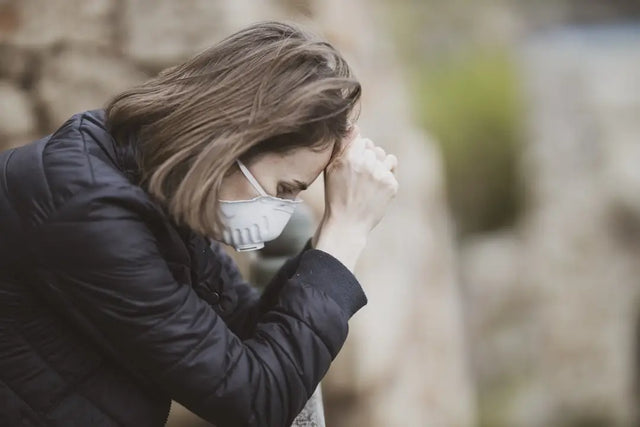 Person in a face mask and winter jacket expresses distress related to mental health awareness.