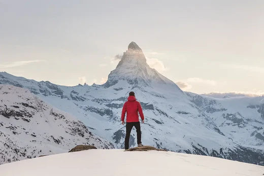 Person in red jacket on snowy peak with Matterhorn, embodying growth mindset and hustle culture.