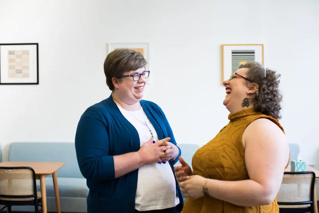 Two colleagues sharing a joyful moment in a positive work environment conversation.