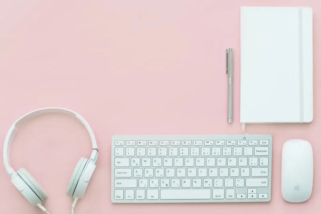 Mint green headphones, white keyboard and mouse on pink surface reflecting digital age trends.