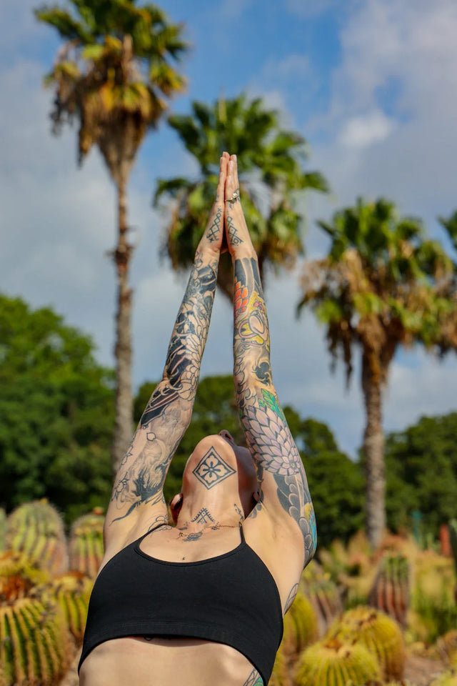 Person with tattooed arms in black sports bra demonstrating yoga pose for flexible culture