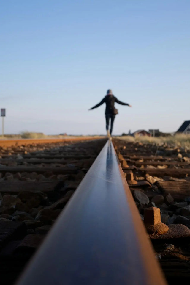 Silhouetted figure balancing on a railway track symbolizing setting boundaries for healthier work-life integration.