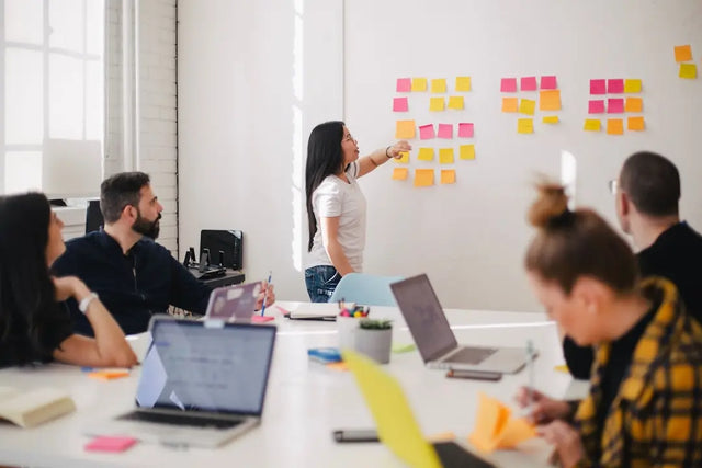 Woman pointing to sticky notes on wall, enhancing communication in hustle culture.