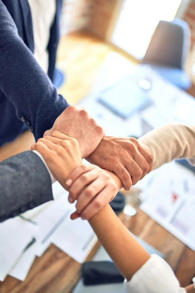 Multiple hands stacked together symbolizing teamwork in conflict resolution for a positive work environment.