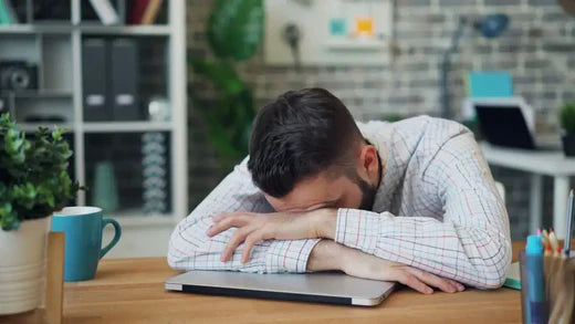 Person resting head on an open book at a wooden table for managing stress techniques.