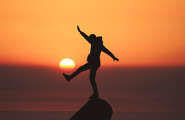 Silhouetted figure balancing atop a rock, symbolizing work-life balance in hustle culture.