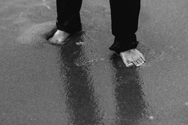 Person’s bare feet and lower legs in dark pants standing in shallow water for personal growth