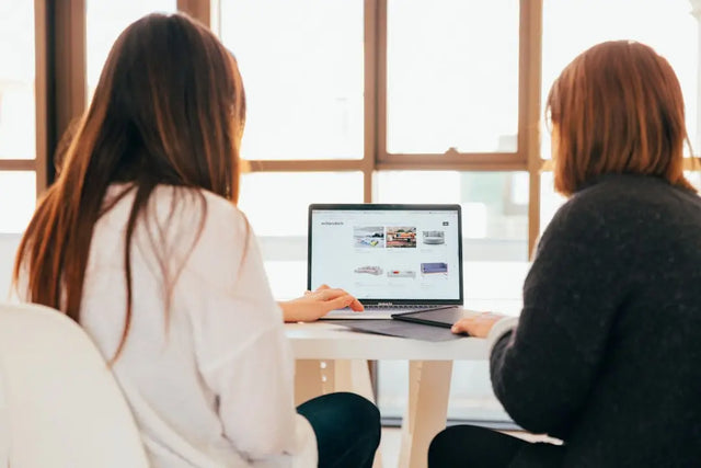 Two colleagues collaborating on a laptop to enhance professional wellbeing amid hustle culture.