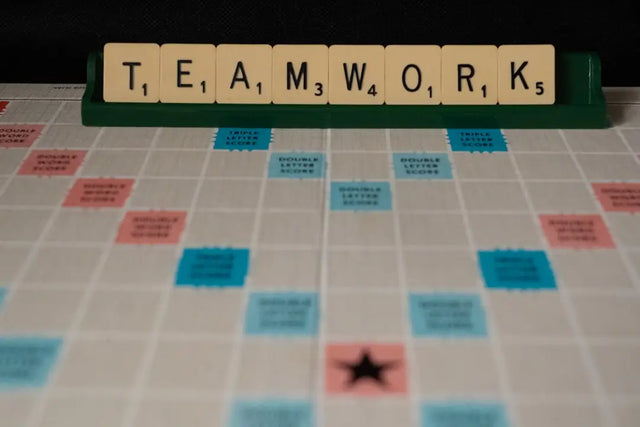 Scrabble tiles forming the word TEAMWORK on a game board, symbolizing a positive work environment.