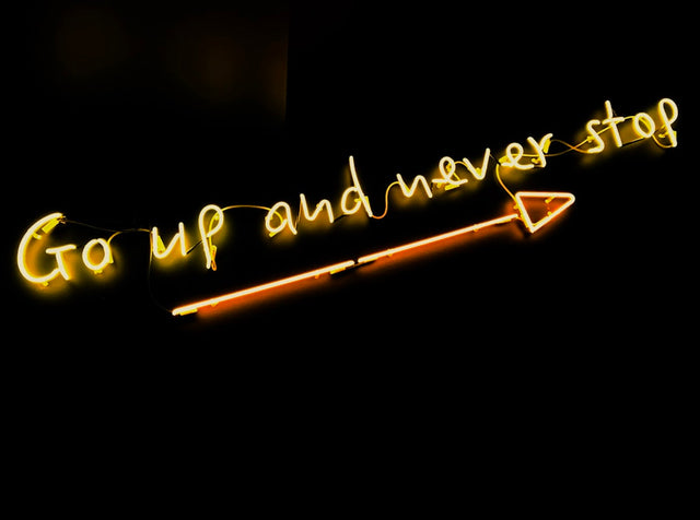 Glowing yellow neon sign promoting healthy habits with the message Go up and never stop.