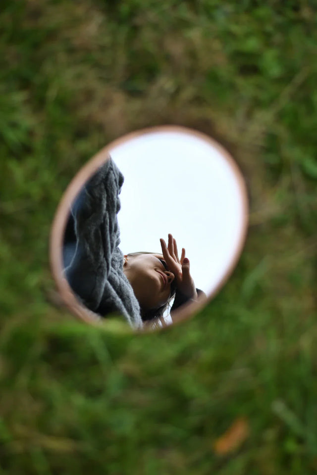 Small oval mirror with a person’s reflection symbolizing self-awareness in hustle culture