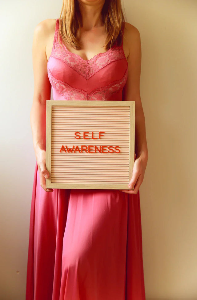 Woman in long pink dress holding a letter board promoting personal growth and self-awareness
