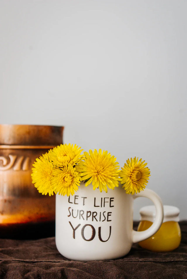 White ceramic mug filled with yellow dandelions symbolizing positive attitude and Avodah Dynamics
