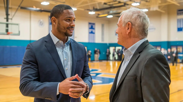 Two men in business attire discussing alumni engagement on a basketball court.