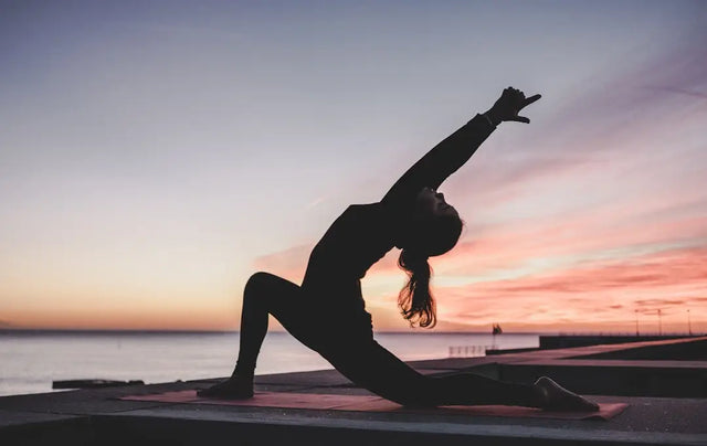 Silhouetted figure in yoga pose at sunset, reflecting physical health and mental wellbeing.