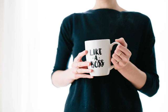 White coffee mug with LIKE A BOSS text held in front of a dark sweater, enhancing enrollment.