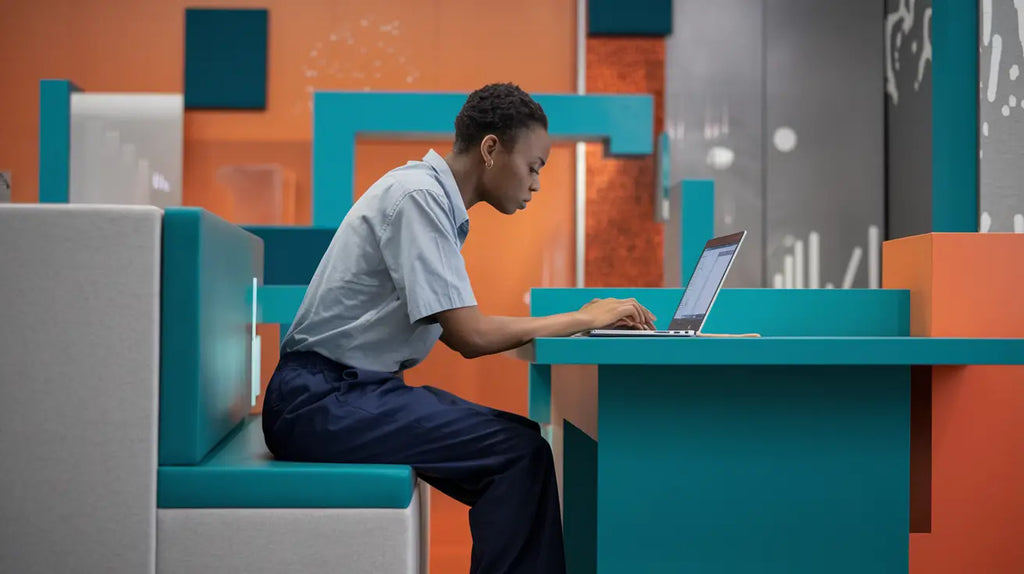 Person at a turquoise booth focused on a laptop, embodying career advancement blueprint.