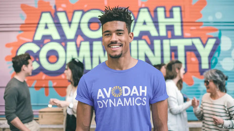 Person smiling in a purple Avodah Dynamics t-shirt, promoting hustle culture and financial independence.