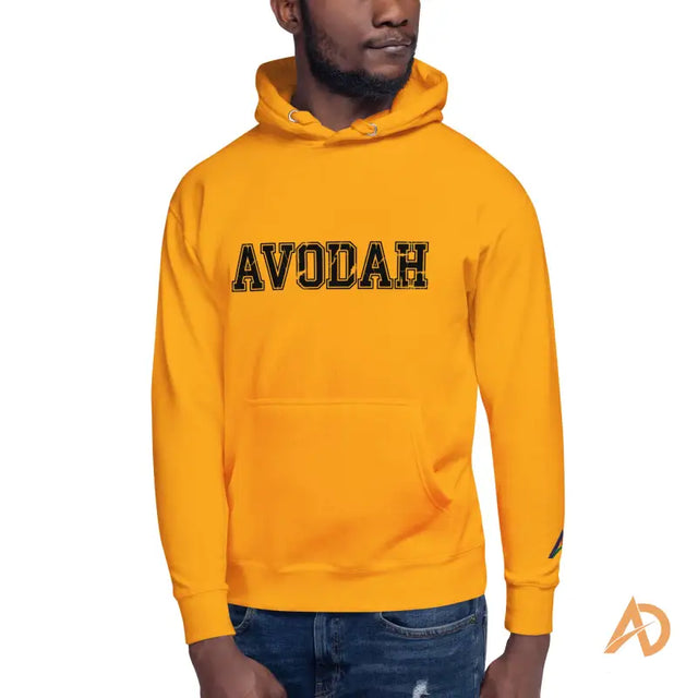 Gold Avodah Varsity Hoodie with black avodah text designMan wearing bright yellow AVODAH hoodie with bold black lettering and blue ripped jeans.