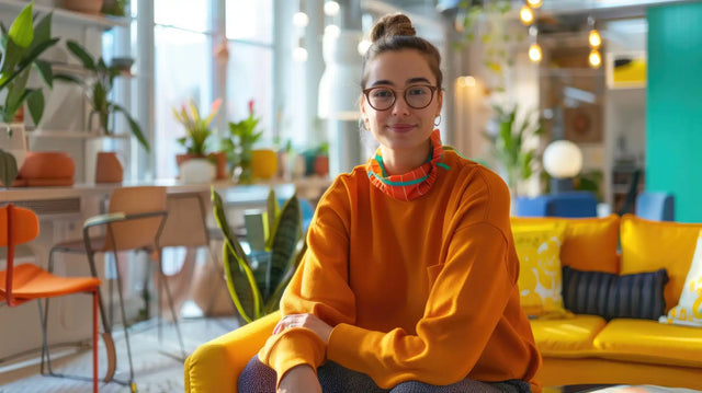 Someone wearing a bright orange sweater and glasses sits on a yellow couch.