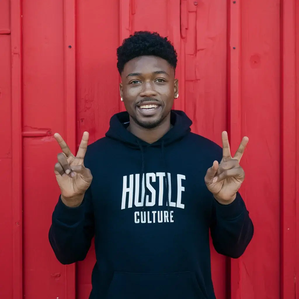 Person in a black Hustle Culture hoodie demonstrating peace signs, embodying transformational leadership.